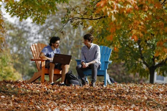 两个学生坐在五颜六色的阿迪朗达克椅子上，周围是秋天的树叶 